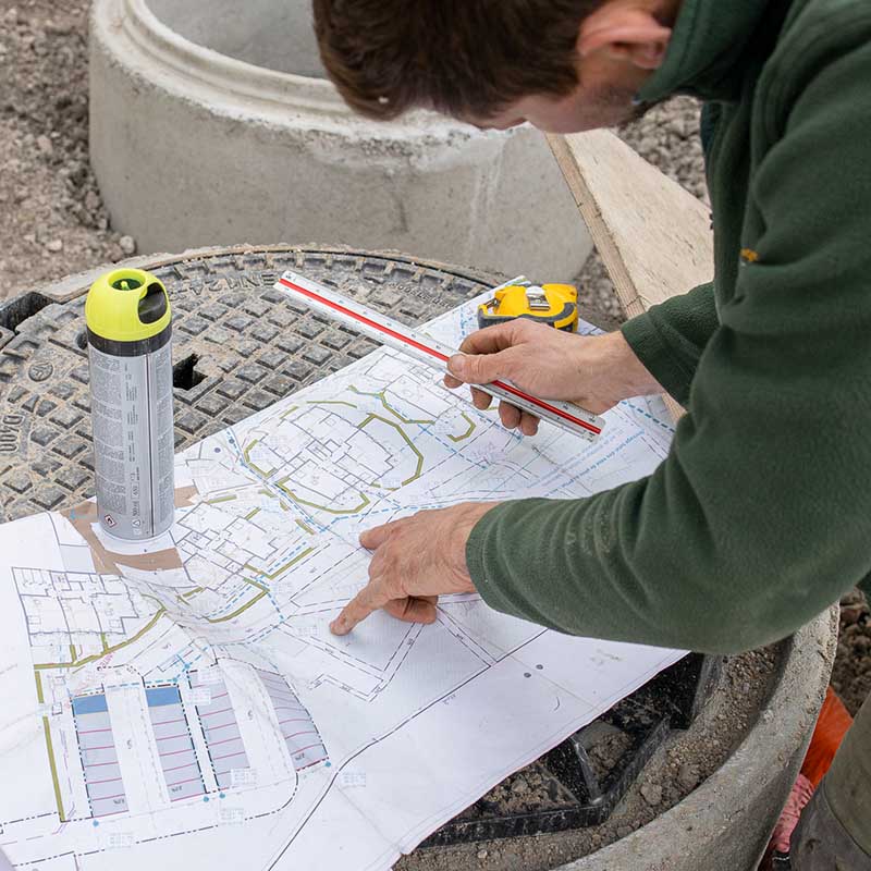 Photographe BTP Marseille : gros plan d'un chef de chantier vérifiant un plan de masse sur un regard en béton.