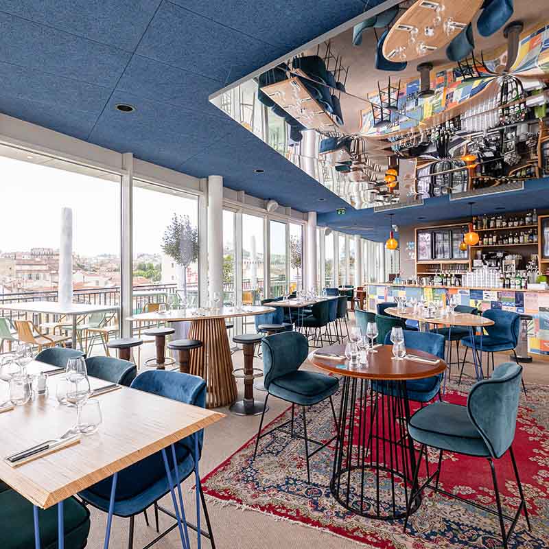 Photographe restaurants Marseille : salle de restaurant design, chaises en velours bleu et vue panoramique sur la ville en PACA.