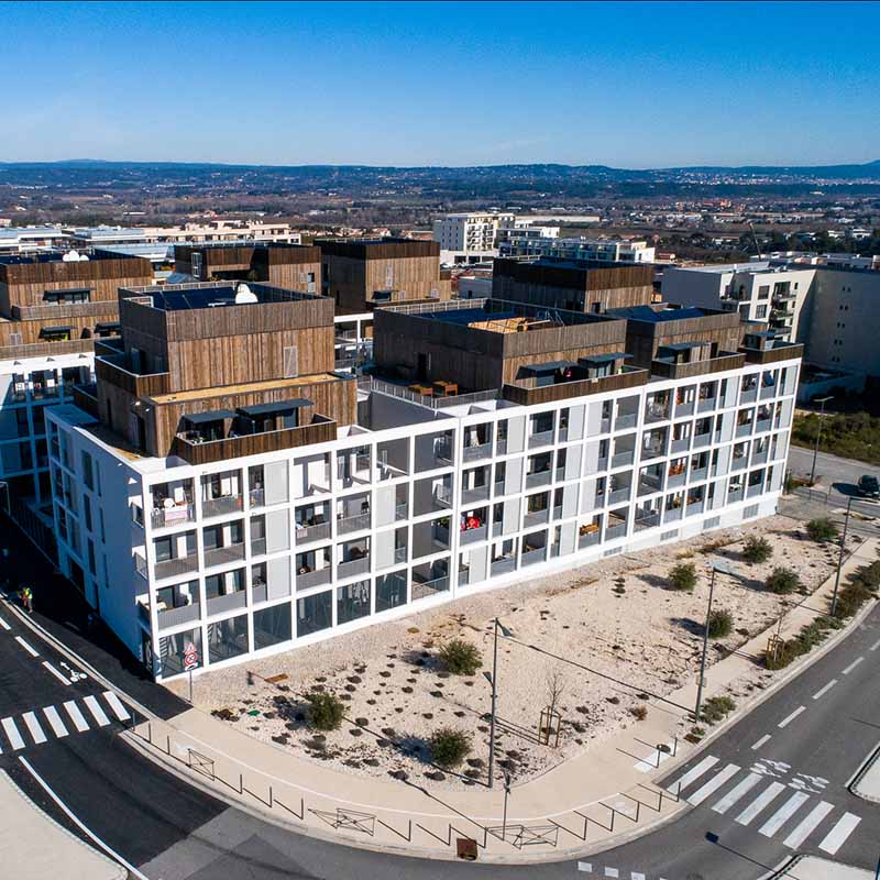 Photo aérienne par drone d'un immeuble résidentiel moderne à Marseille, façades blanches et toits en bois, suivi de chantier.