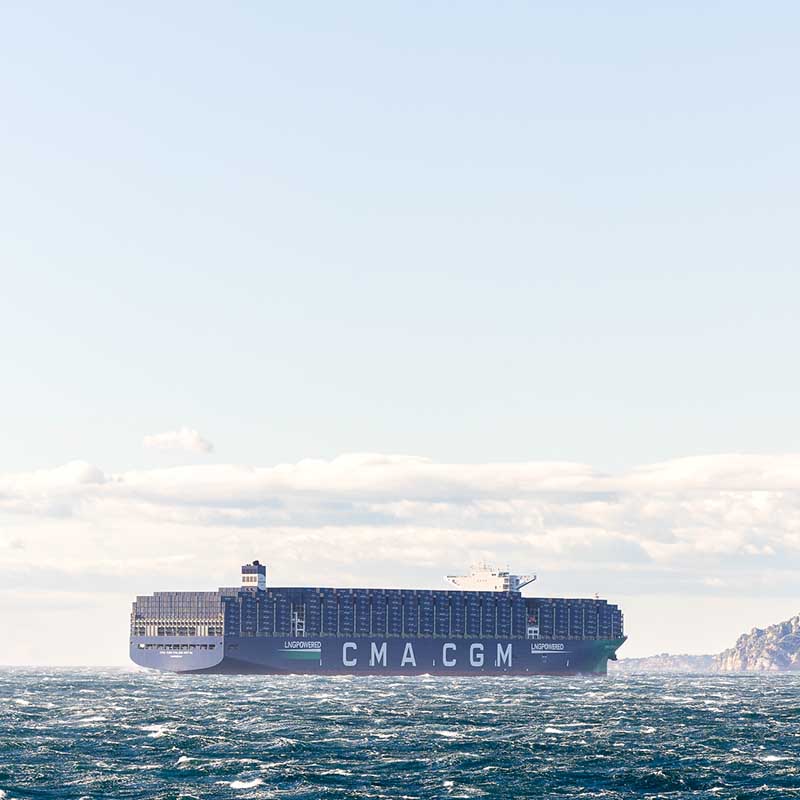 Photo industrielle Marseille : porte-conteneurs géant CMA CGM en navigation dans la rade sous un ciel bleu avec quelques nuages.