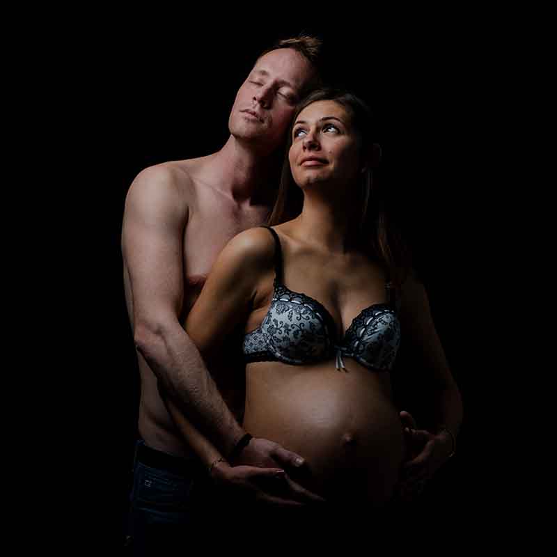 Photographe grossesse Marseille : couple en studio, femme enceinte et mari posant sur fond noir en PACA.