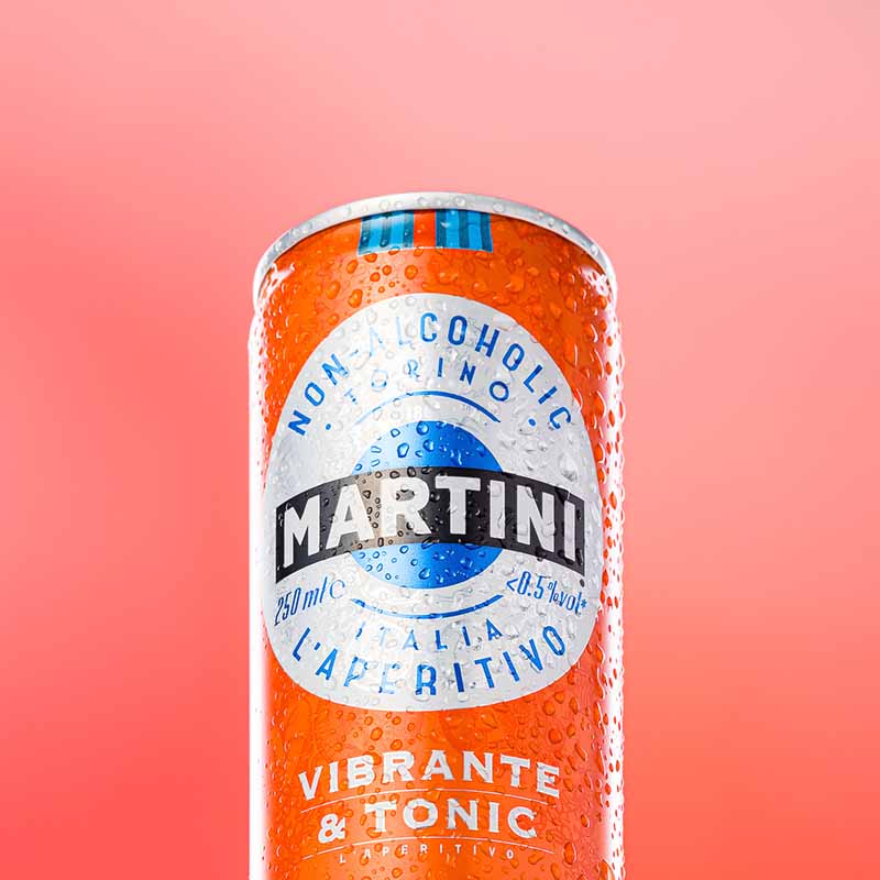 Photographie packshot d'une canette Martini Vibrante & Tonic fraîche avec gouttelettes d'eau sur fond corail uni.