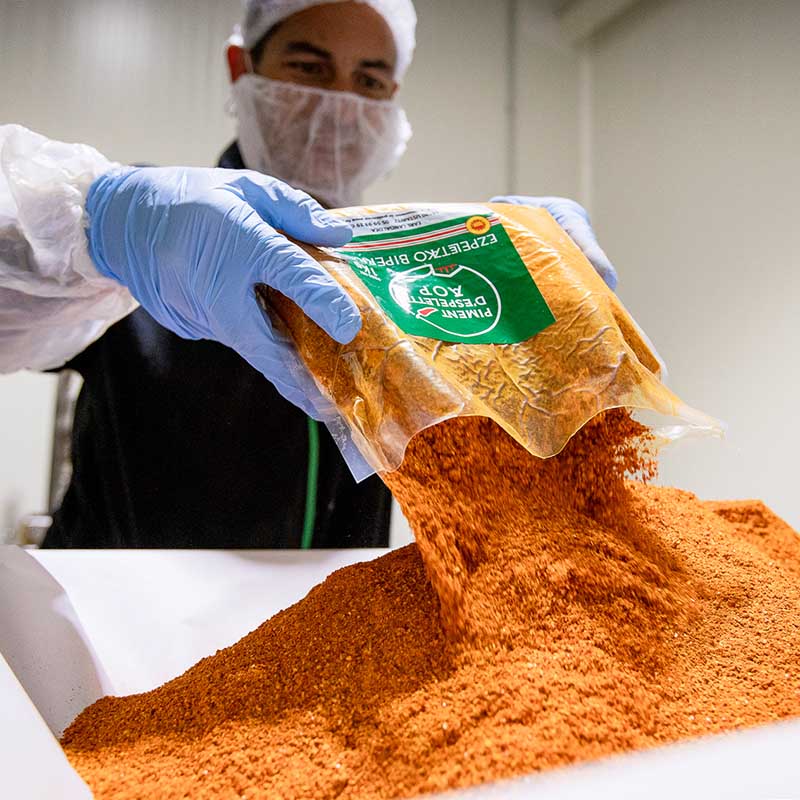 Photo industrie agroalimentaire Marseille : un ouvrier ganté verse un sac de piment d'Espelette AOP dans un bac de mélange.