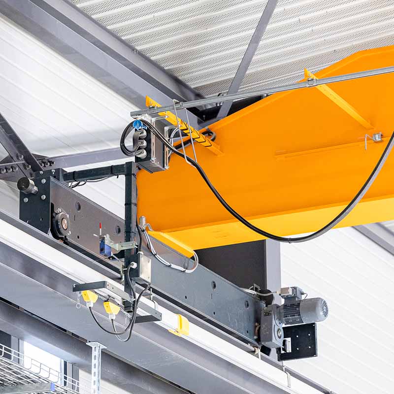 Photo industrielle Marseille : détail technique d'un pont roulant de levage jaune et gris installé sous la charpente d'un dépôt.