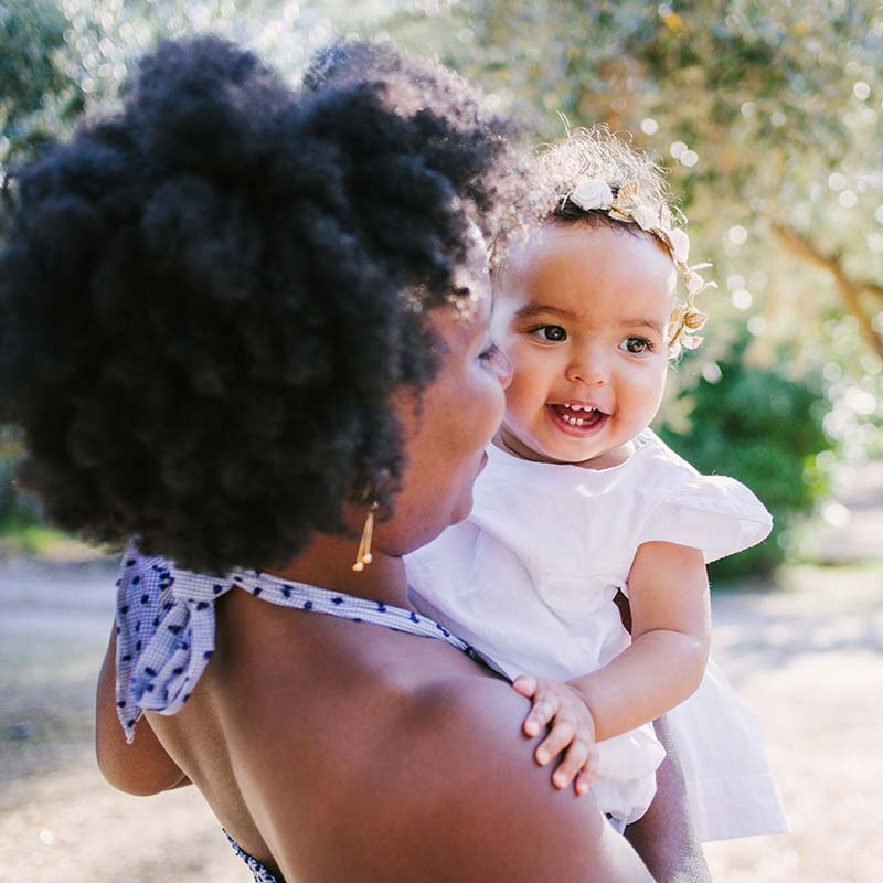Photographe famille Marseille : maman tenant son bébé souriant dans ses bras dans un jardin ensoleillé en PACA.