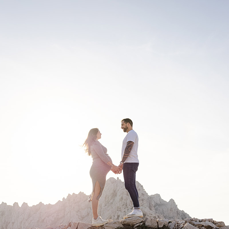 Photographe grossesse Marseille : couple attendant un enfant sur une crête rocheuse face aux montagnes.