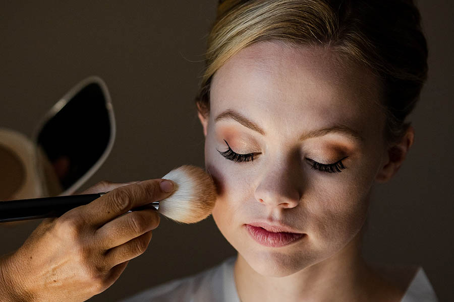 Gros plan sur une mariée aux yeux clos pendant l'application de son maquillage par une professionnelle lors des préparatifs du mariage à Marseille.